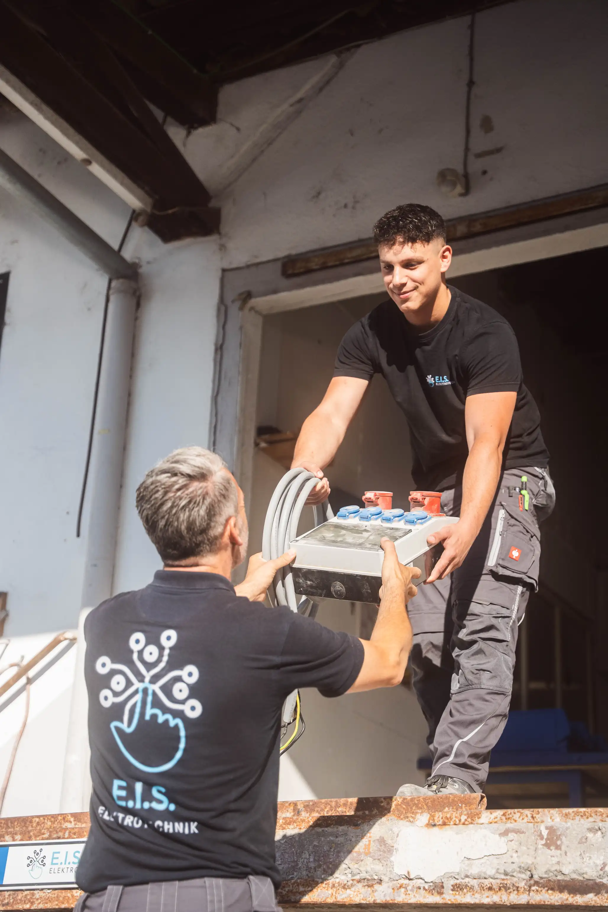 Zwei Monteure heben einen Verteiler an — E.I.S Elektrotechnik
